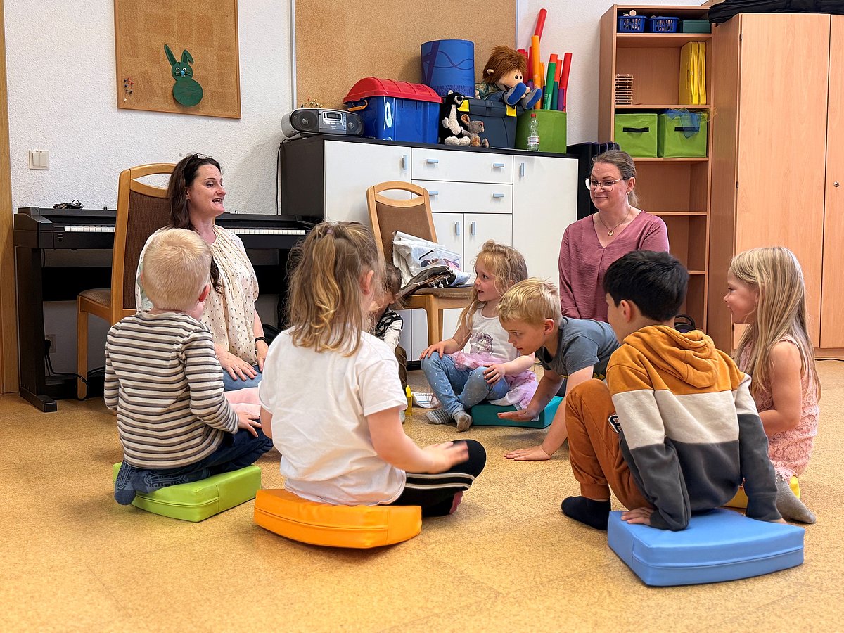 Kinder sitzen im Kreis am Boden und singen